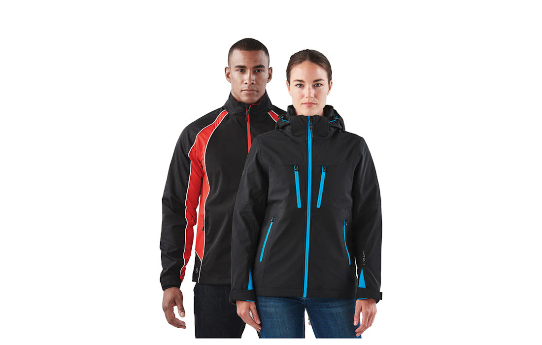 A man and a woman modeling black outdoor jackets against a plain white background. The woman in front wears a black jacket with bright blue zipper accents, and the man behind her wears a black jacket with red and white side panels.